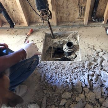 A neatly cut opening in a concrete slab exposing the drain line underneath during a repair.