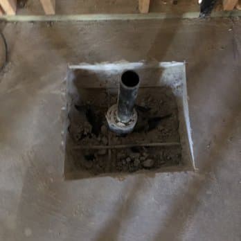 A drain stub-out rising from a freshly poured patch in a concrete slab.